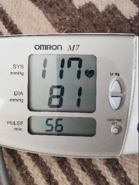 Upper-arm blood pressure monitor screen showing systolic 117, diastolic 81 and pulse 56